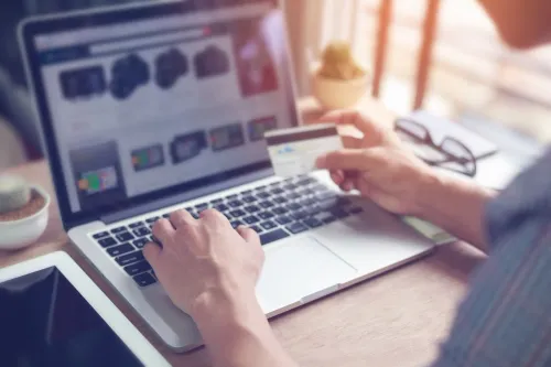 Close up of man's hands typing on a computer and holding a credit card